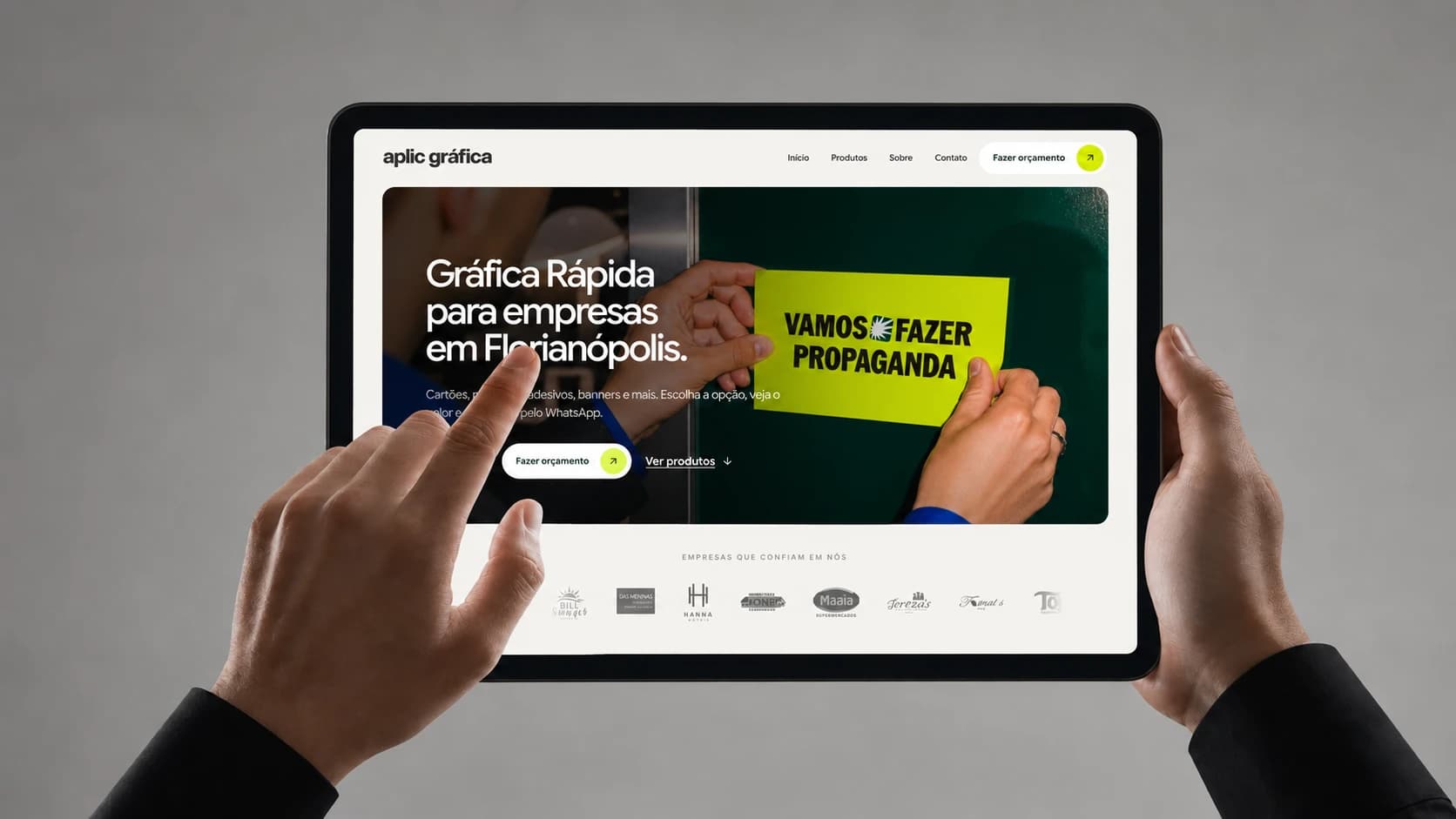 Website da Aplic Gráfica em um tablet segurado com as duas mãos